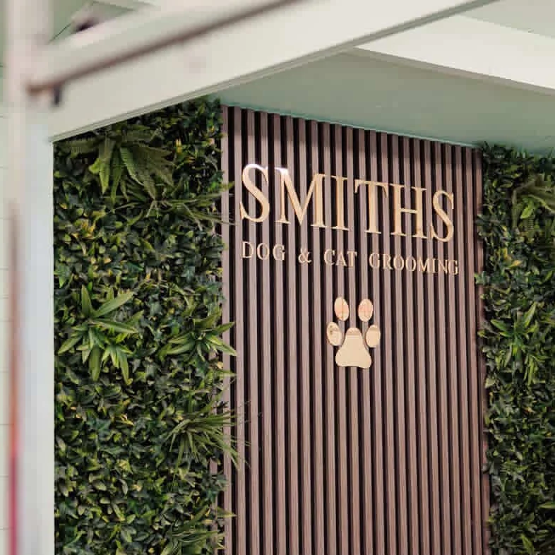 The Smiths Dog & Cat Grooming sign on a slatted wall between panels of greenery